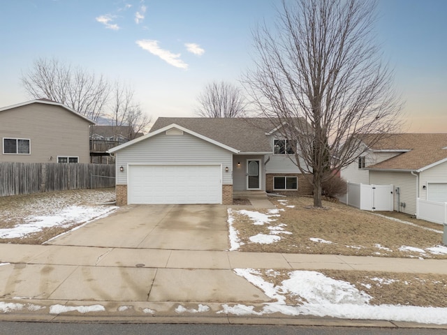 tri-level home with brick siding, an attached garage, driveway, and fence