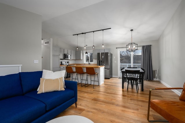 living room featuring visible vents, track lighting, baseboards, vaulted ceiling, and light wood-style floors