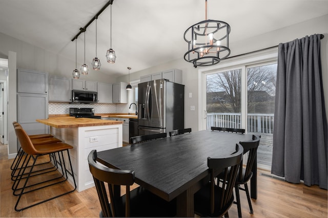 dining area featuring visible vents, light wood finished floors, a notable chandelier, and vaulted ceiling