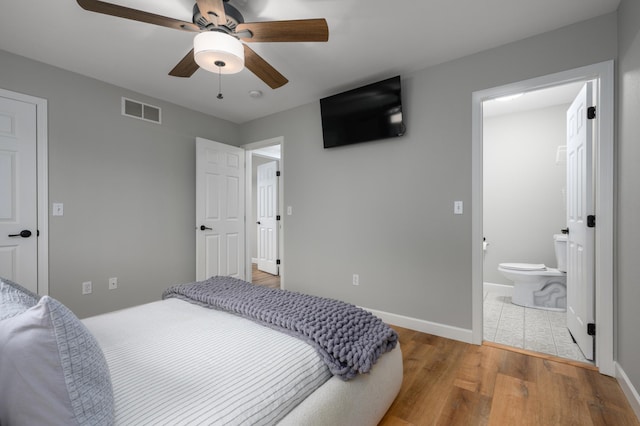 bedroom with visible vents, a ceiling fan, ensuite bathroom, wood finished floors, and baseboards