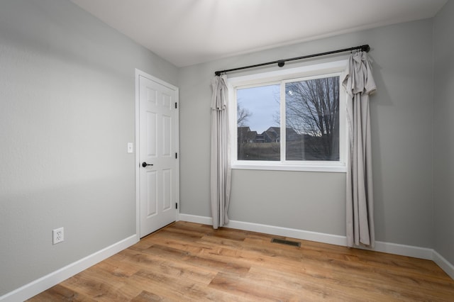 unfurnished room featuring light wood finished floors, visible vents, and baseboards