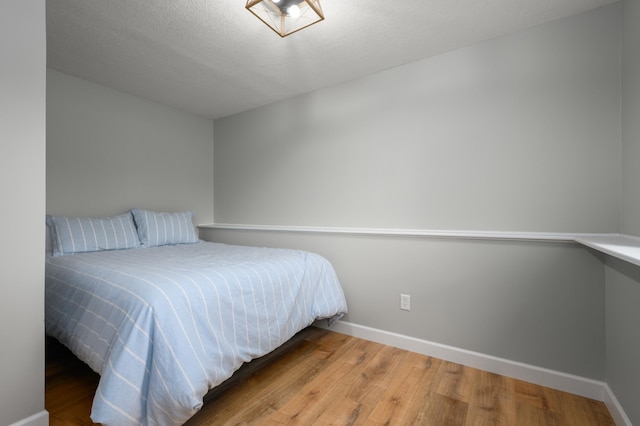 bedroom with a textured ceiling, baseboards, and wood finished floors