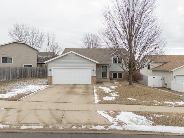 split level home featuring a garage, fence, brick siding, and driveway