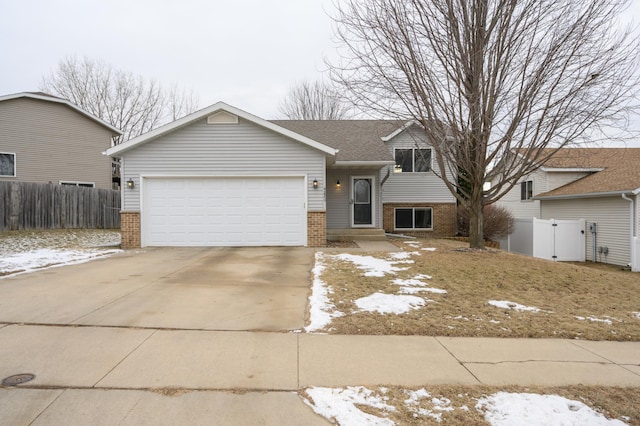 split level home with brick siding, an attached garage, and fence