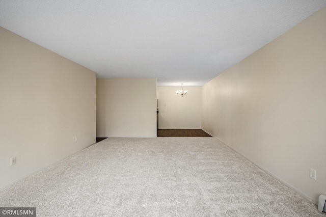 empty room with a notable chandelier, baseboard heating, and carpet flooring