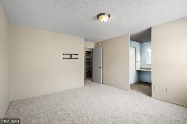 unfurnished bedroom with connected bathroom, a spacious closet, carpet floors, and a textured ceiling