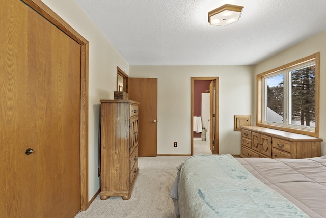 bedroom with connected bathroom, light colored carpet, and a textured ceiling