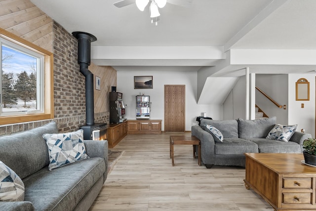 living room featuring brick wall, light hardwood / wood-style flooring, ceiling fan, and a wood stove