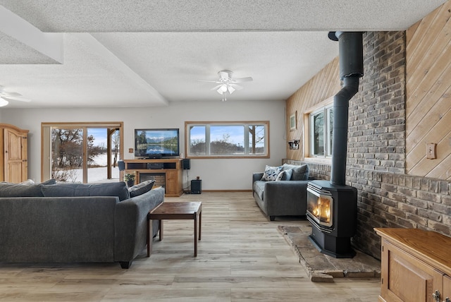 living room featuring ceiling fan, a healthy amount of sunlight, light hardwood / wood-style flooring, and a wood stove