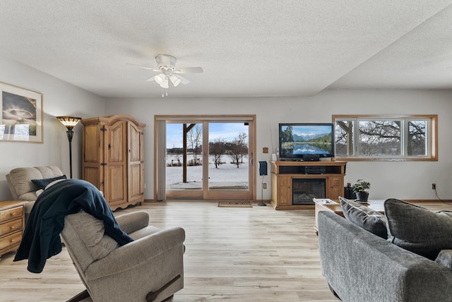 living room featuring ceiling fan, a textured ceiling, and light wood-type flooring