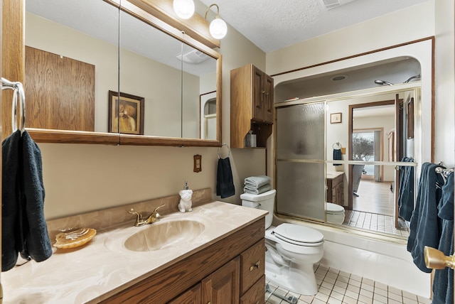 full bathroom with shower / bath combination with glass door, tile patterned flooring, vanity, a textured ceiling, and toilet