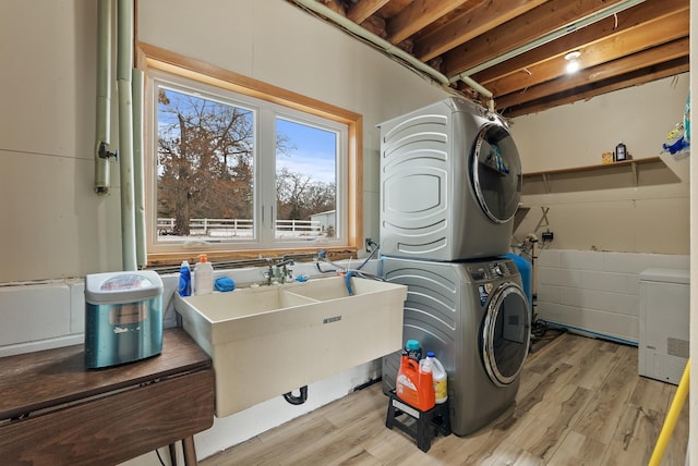 clothes washing area with stacked washing maching and dryer, sink, and light wood-type flooring