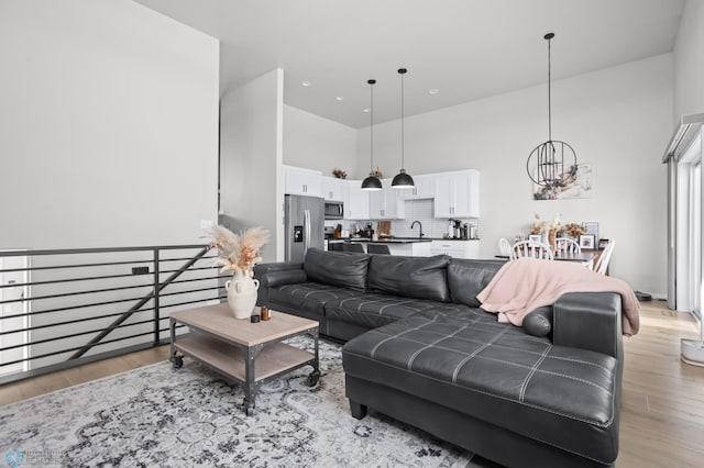 living room with a towering ceiling, sink, a chandelier, and light hardwood / wood-style flooring