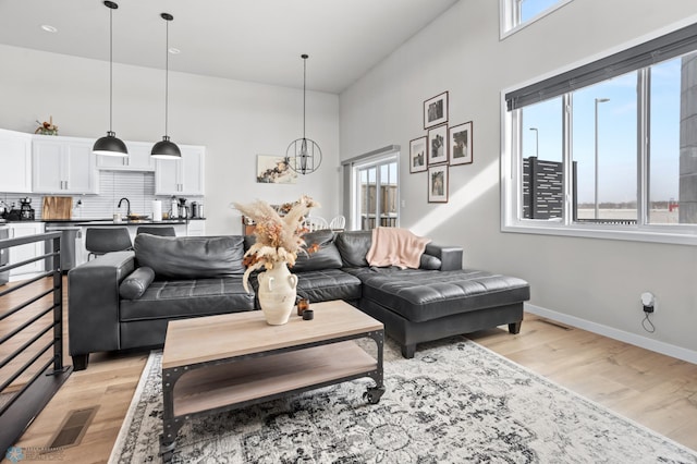 living room featuring sink, a chandelier, light hardwood / wood-style floors, and a high ceiling