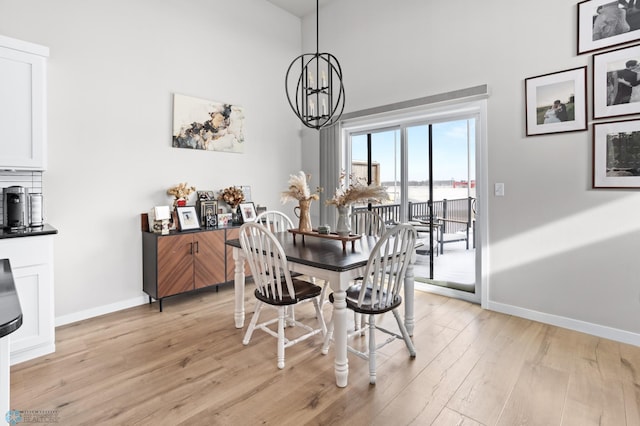 dining room featuring a notable chandelier, a towering ceiling, and light wood-type flooring