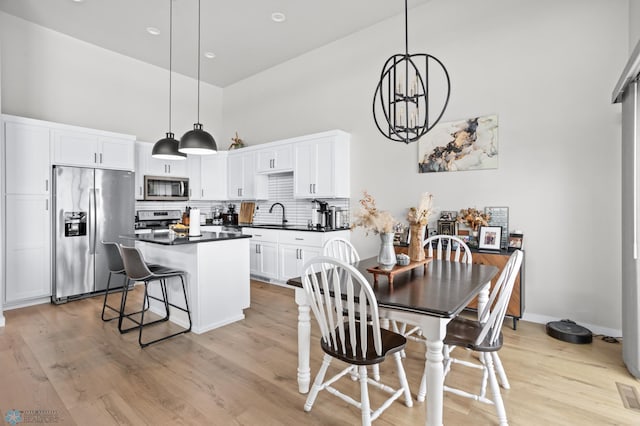 kitchen with sink, white cabinetry, pendant lighting, stainless steel appliances, and a high ceiling