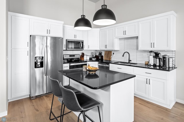 kitchen featuring white cabinetry, sink, a kitchen breakfast bar, hanging light fixtures, and stainless steel appliances