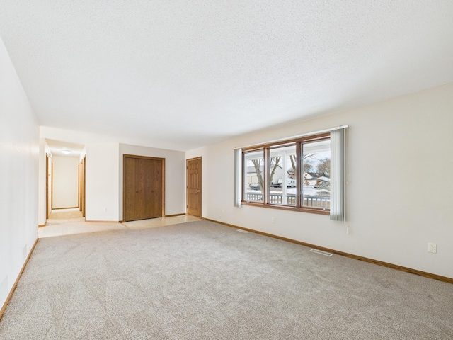 unfurnished room featuring light colored carpet, a textured ceiling, and baseboards