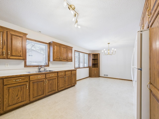 kitchen with a sink, brown cabinets, freestanding refrigerator, and a chandelier