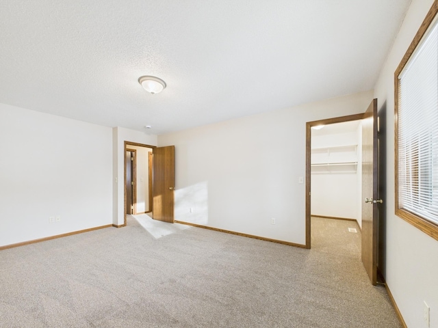 unfurnished bedroom featuring baseboards, light carpet, a closet, and a spacious closet