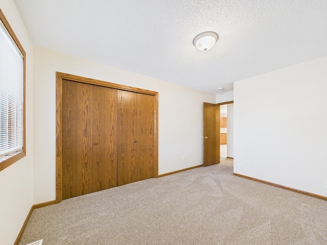 unfurnished bedroom featuring a textured ceiling, baseboards, a closet, and light carpet