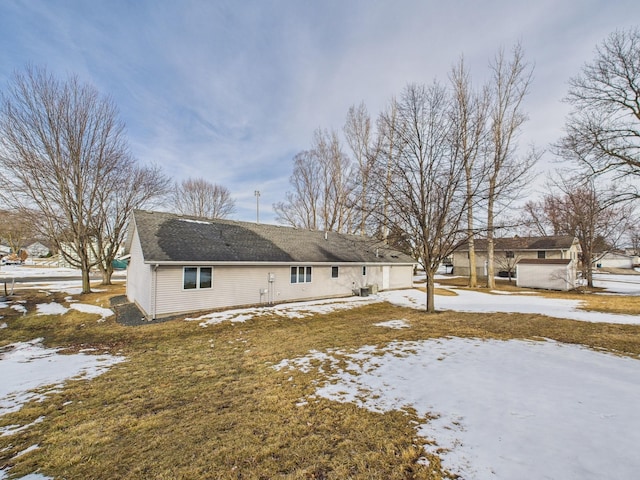 snow covered rear of property with concrete driveway, an attached garage, and a shingled roof