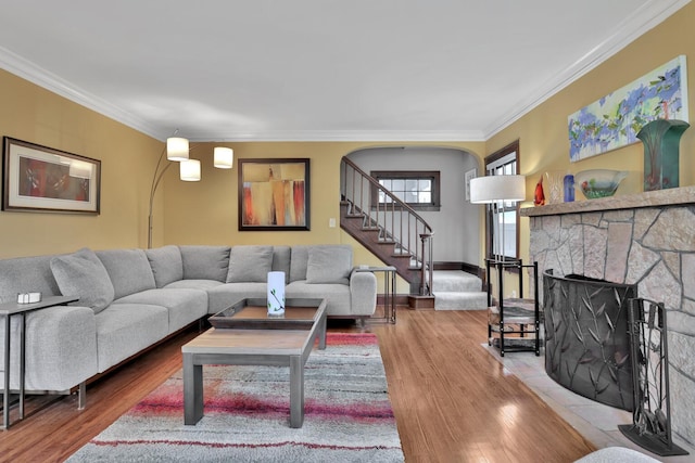 living room featuring crown molding, wood-type flooring, and a stone fireplace