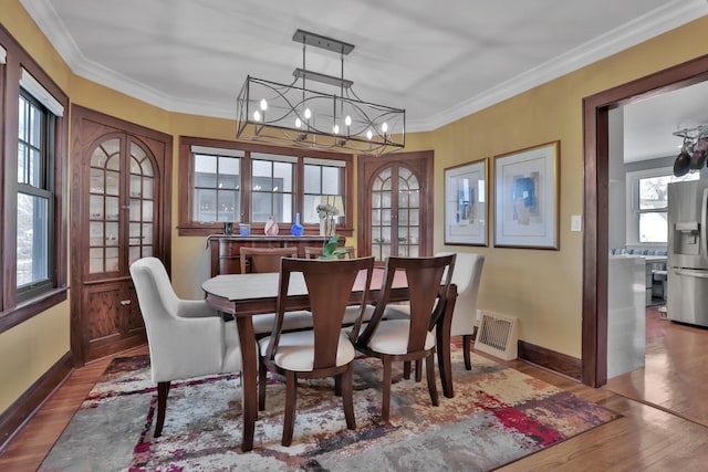 dining area with wood-type flooring, ornamental molding, and french doors