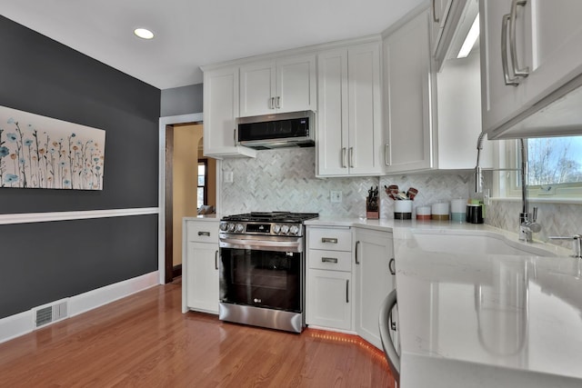 kitchen featuring backsplash, appliances with stainless steel finishes, light wood-type flooring, and white cabinets