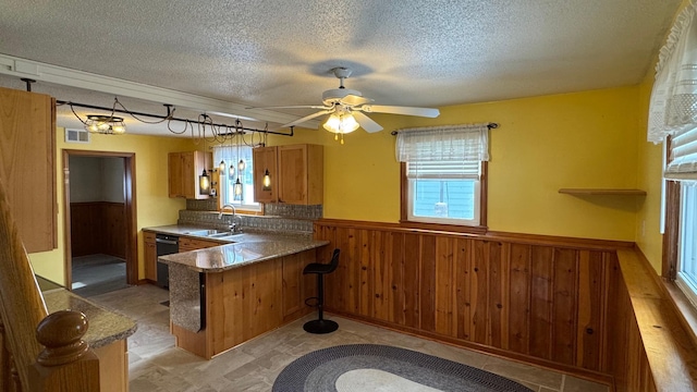 kitchen featuring wooden walls, black dishwasher, sink, kitchen peninsula, and a textured ceiling