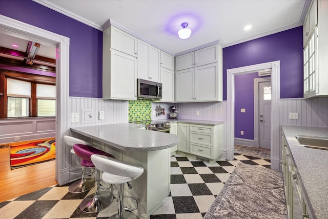 kitchen with dark floors, stainless steel appliances, wainscoting, a kitchen bar, and crown molding