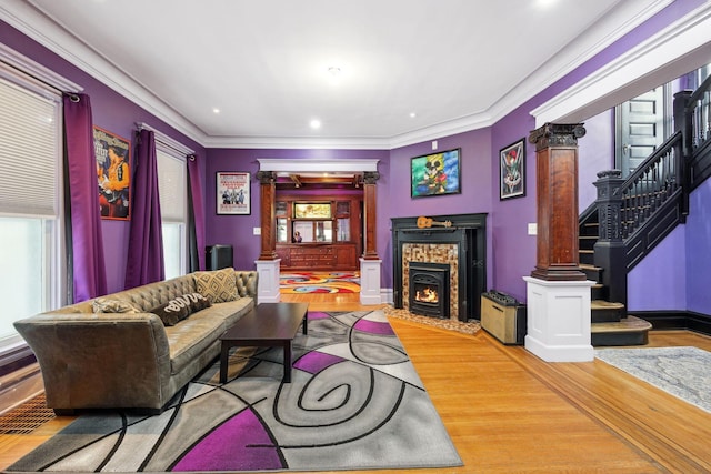 living room with ornamental molding, a fireplace with flush hearth, wood finished floors, ornate columns, and stairs