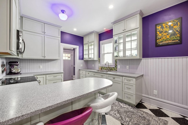 kitchen featuring light countertops, stainless steel microwave, glass insert cabinets, a sink, and a kitchen bar