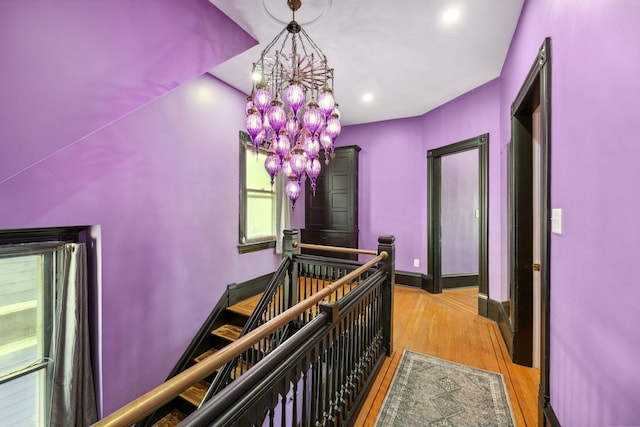 corridor with a chandelier, baseboards, light wood-style flooring, and an upstairs landing