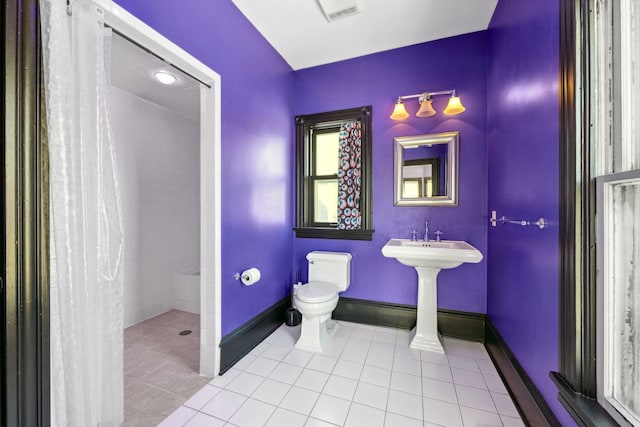 bathroom with baseboards, a tile shower, toilet, and tile patterned floors