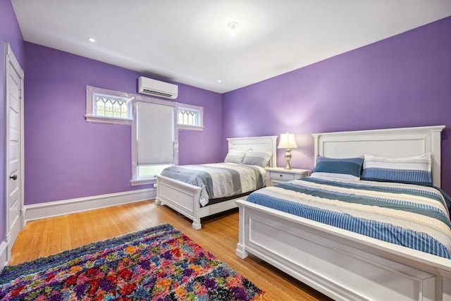 bedroom featuring a wall mounted AC, light wood-style flooring, and baseboards