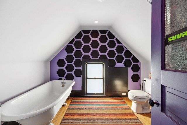 full bath featuring lofted ceiling, a soaking tub, toilet, and wood finished floors