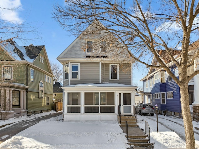 snow covered rear of property featuring a sunroom