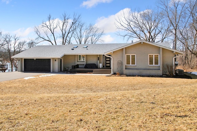 ranch-style house featuring brick siding, concrete driveway, a front yard, central AC unit, and an attached garage