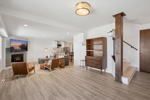 living area featuring baseboards, stairs, light wood-type flooring, recessed lighting, and a glass covered fireplace