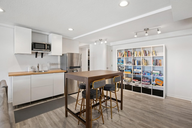 kitchen with a sink, stainless steel appliances, light wood-style floors, a textured ceiling, and white cabinetry