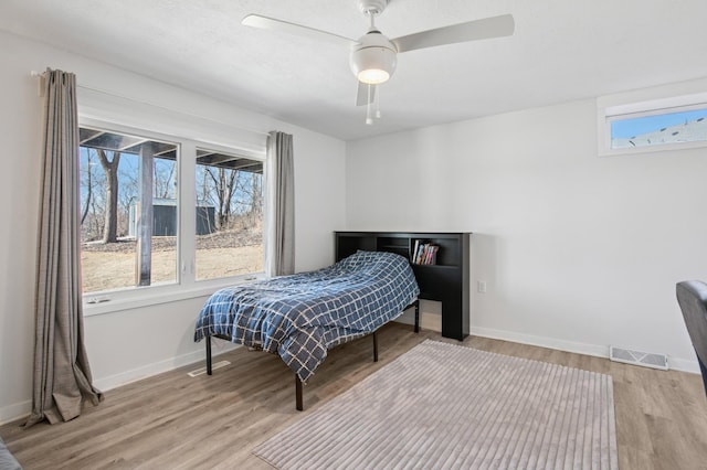 bedroom featuring ceiling fan, visible vents, baseboards, and wood finished floors