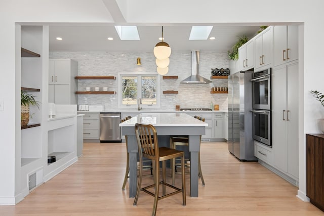 kitchen with open shelves, wall chimney range hood, a skylight, and appliances with stainless steel finishes