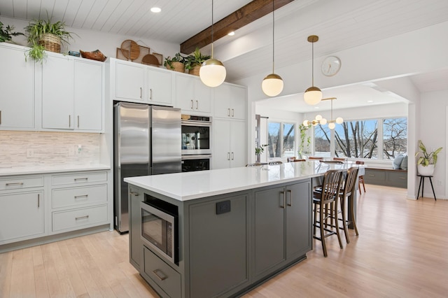 kitchen with light wood-style flooring, gray cabinetry, light countertops, appliances with stainless steel finishes, and backsplash