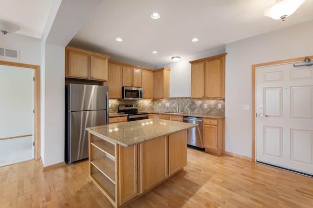 kitchen featuring visible vents, light wood-style flooring, a center island, stainless steel appliances, and backsplash