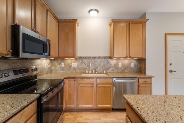 kitchen with light stone counters, light wood finished floors, stainless steel appliances, tasteful backsplash, and a sink