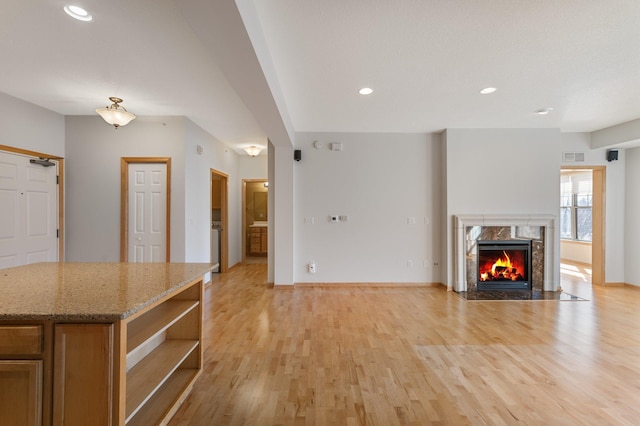 unfurnished living room with light wood finished floors, visible vents, baseboards, a high end fireplace, and recessed lighting