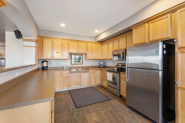 kitchen featuring appliances with stainless steel finishes, a peninsula, light brown cabinets, a sink, and recessed lighting