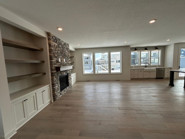 unfurnished living room with built in features, a sink, a stone fireplace, a textured ceiling, and wood finished floors