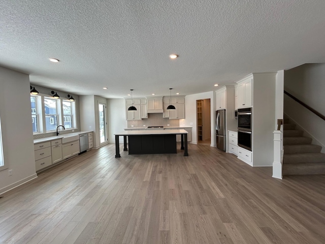 kitchen featuring a large island, decorative light fixtures, stainless steel appliances, light countertops, and a sink